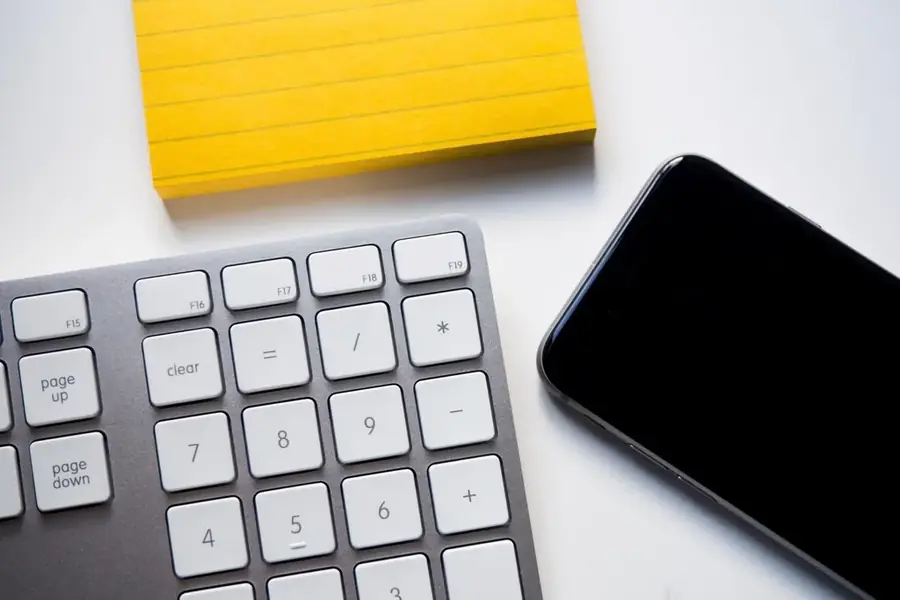 A yellow notepad, a numeric keypad and a phone on a plain white desk